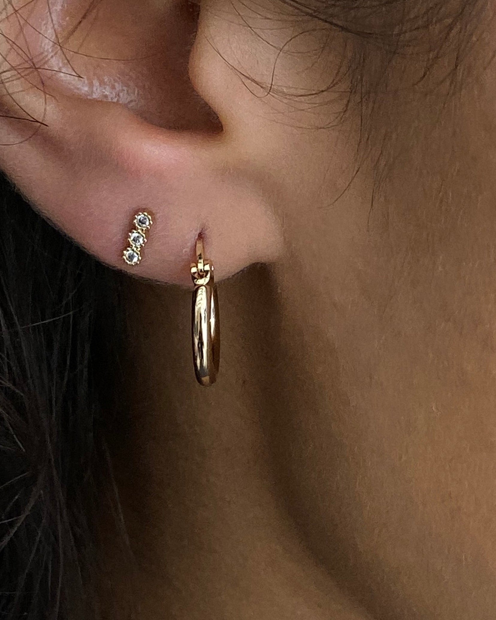 Close-up of an ear wearing gold hoop earrings with a blurred background